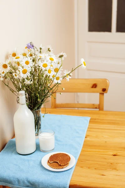 Simply stylish wooden kitchen with bottle of milk and glass on table, summer flowers camomile, healthy food moring concept