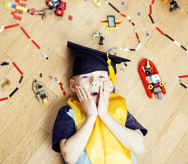 Little cute preschooler boy among toys lego at home in graduate hat smiling posing emotional, lifestyle people concept