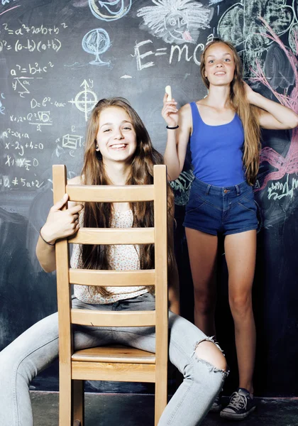 Back to school after summer vacations, two teen real girls in classroom with blackboard painted together