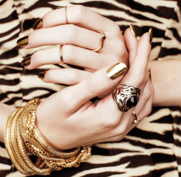 Woman hands with golden manicure lot of jewelry on fancy dress close up