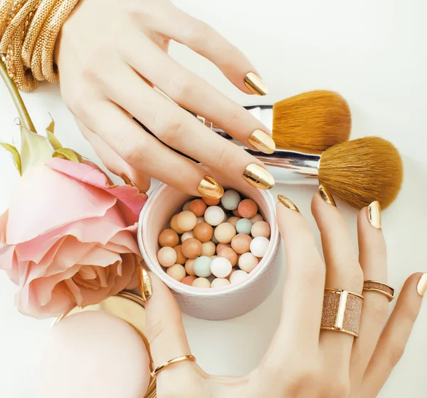 Woman hands with golden manicure and many rings holding brushes, makeup artist stuff stylish, pure close up pink flower rose among cosmetic