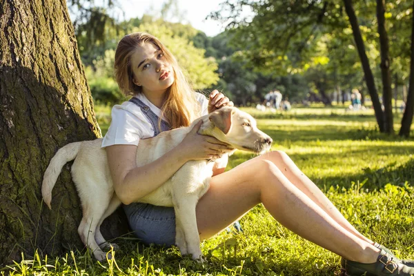 Young attractive blond woman playing with her dog in green park at summer, lifestyle people concept