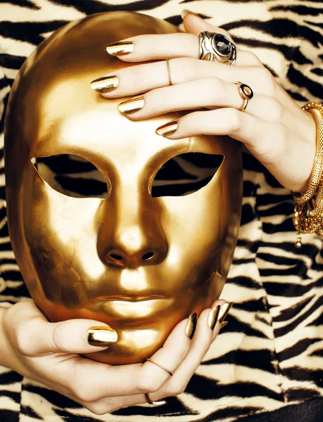 Woman hands holding golden carnival halloween mask, rich luxury manicure and jewelry close up on zebra print, fashion clothers for people