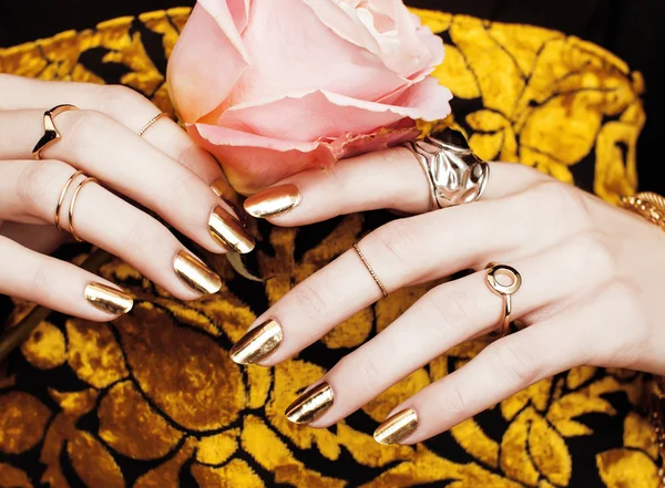 Woman hands with golden manicure lot of jewelry on fancy dress close up
