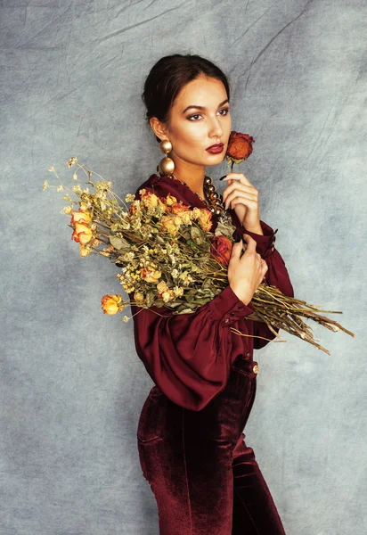 Young attractive stylish brunette woman with bouquet of gorgeous dry roses wearing vinous clothers and gold jewelry, lifestyle autumn people concept,  Renaissance