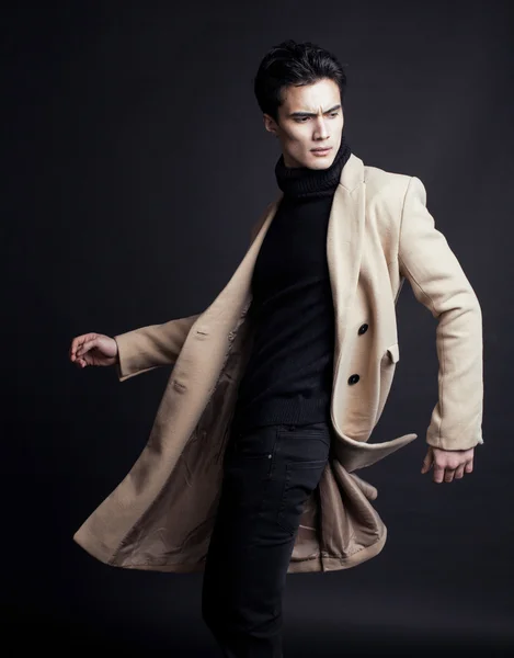 Cool real young man in coat on black background posing