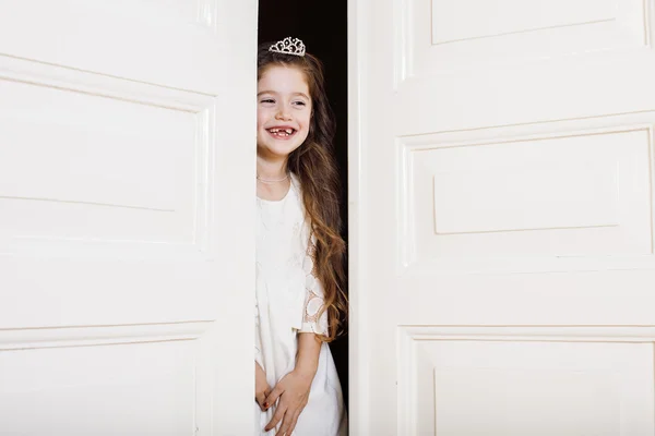 Little cute girl at home, opening door well-dressed in white dress, adorable milk fairy teeth