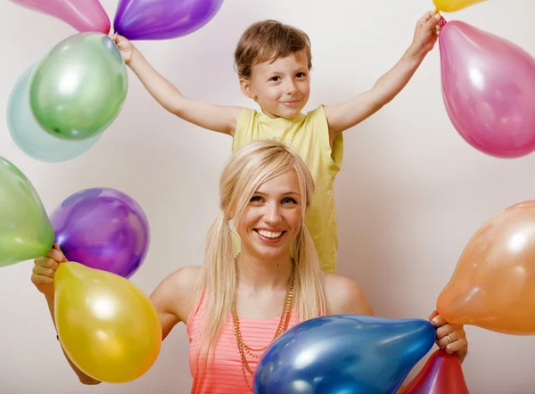 Pretty real family with color balloons on white background, blond woman with little boy at birthday party bright smiling mother