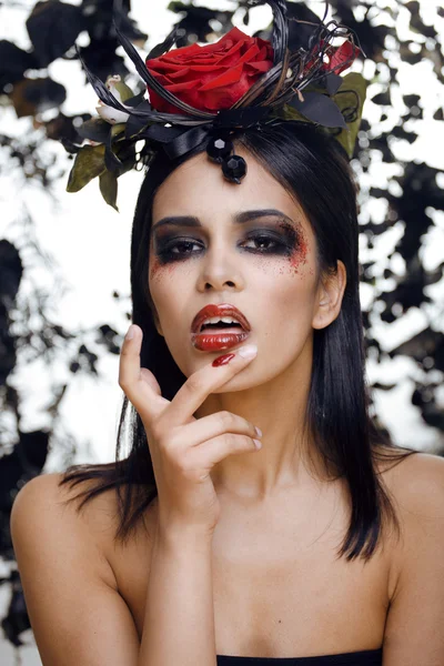 Pretty brunette woman with rose jewelry, black and red, bright make up kike a vampire