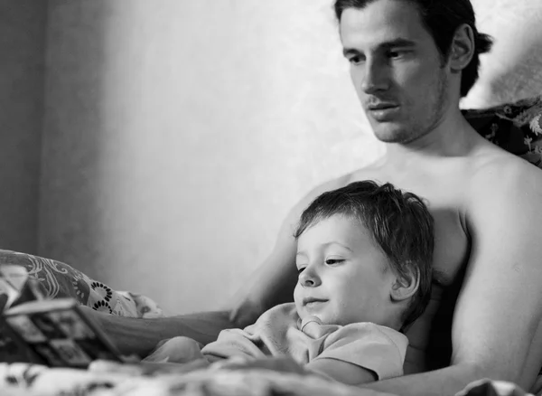 Black and white picture of father with son reading book in bed