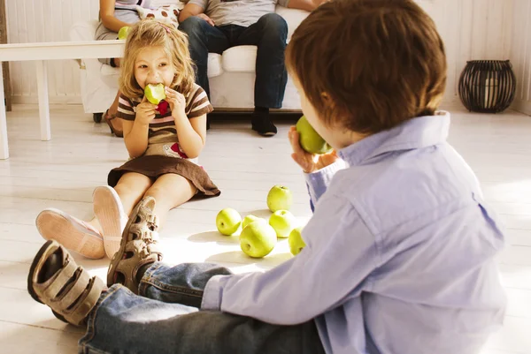 Cute boy and girl eating green apple at home interior
