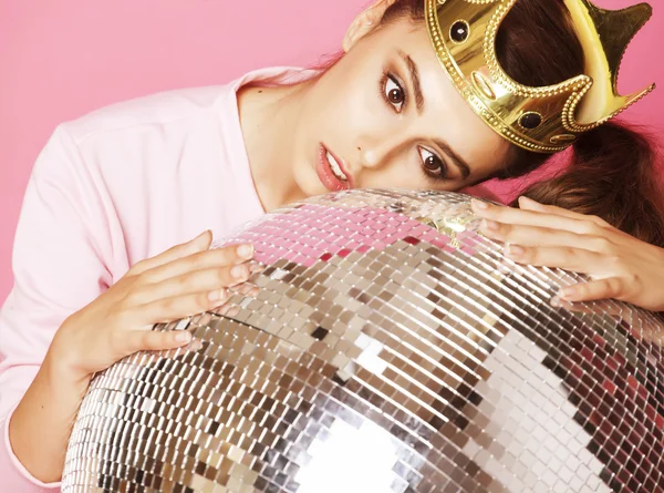 Young cute girl like barbie on pink background with disco ball and crown