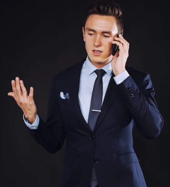 Young pretty business man standing on black background, modern hairstyle, talking on phone