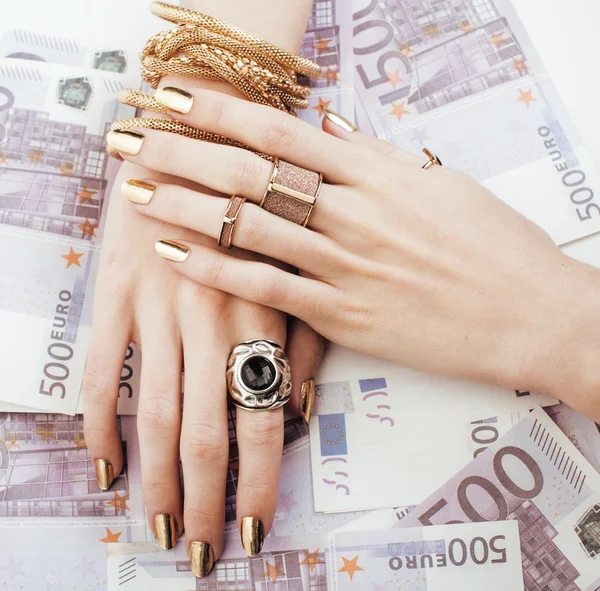 Hands of rich woman with golden manicure and many jewelry rings on cash euros