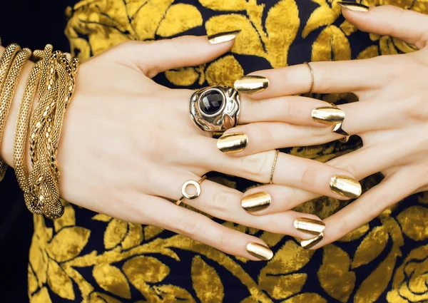 Woman hands with golden manicure lot of jewelry on fancy dress