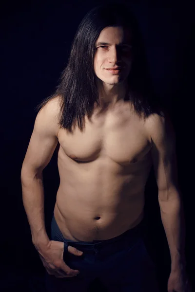 Handsome young man with long hair naked torso on black background