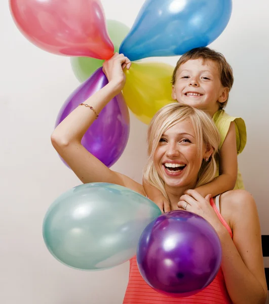 Pretty real family with color balloons on white background, blond woman with little boy at birthday party