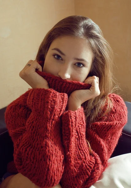 Young pretty real woman in red sweater and scarf all over her face smiling at home, winter positive