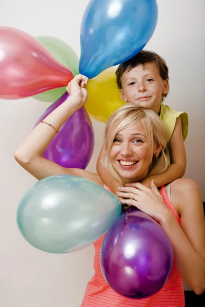 Pretty real family with color balloons on white background, blond woman with little boy on birthday party isolated