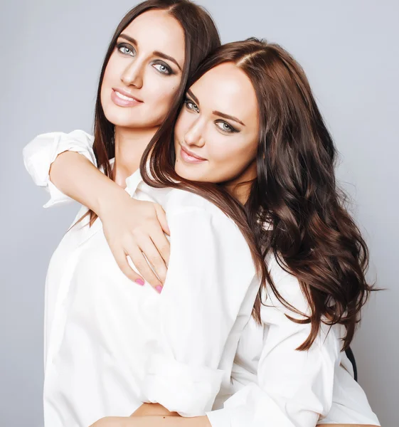 Two sisters twins posing, making photo selfie, dressed same white shirt, diverse hairstyle friends smiling close up