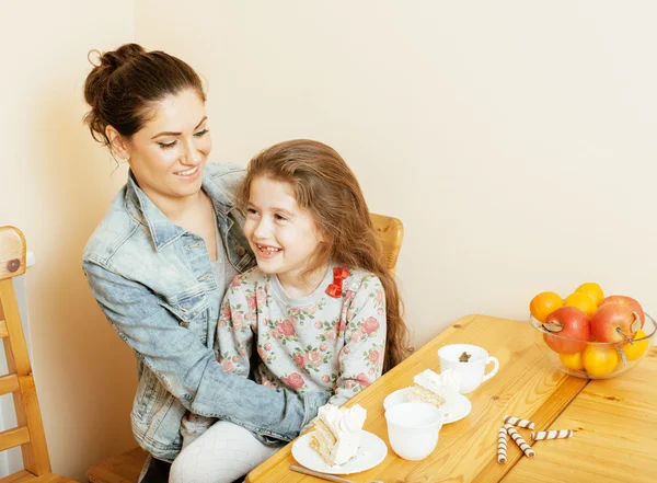 Young mother with daughter on kitchen drinking tea together hugging eating celebration cake smiling, birthday party