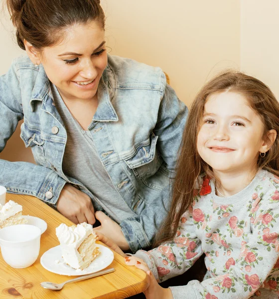 Young mother with daughter on kitchen drinking tea together hugging eating celebration cake birthday