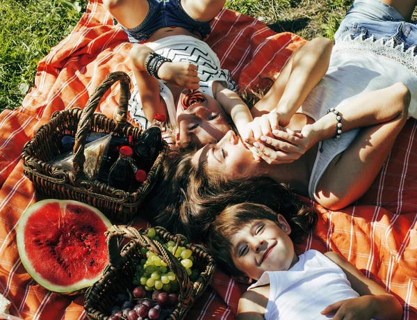 Cute happy family on picnic laying on green grass mother and kids, warm summer vacations close up, brother and sister