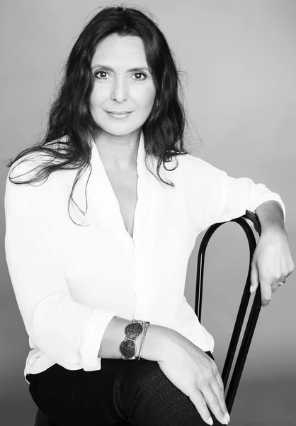 Pretty brunette confident mature woman sitting on chair in studio