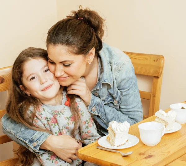 Young mother with daughter on kitchen drinking tea together hugging eating celebration cake