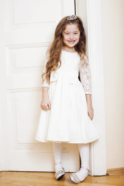 Little cute girl at home, opening door well-dressed in white dress, adorable milk fairy teeth