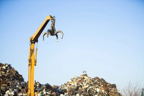 Crane picking up scrap metal in recycling site outdoors