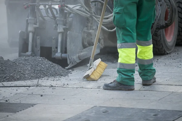 Worker operating asphalt paver machine during road construction and repairing works