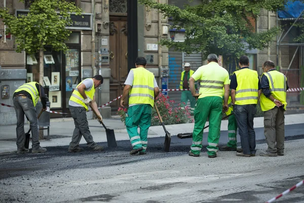 Worker operating asphalt paver machine during road construction and repairing works