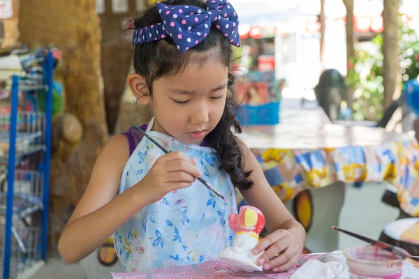 Cute asian girl painting color on the plaster statue.