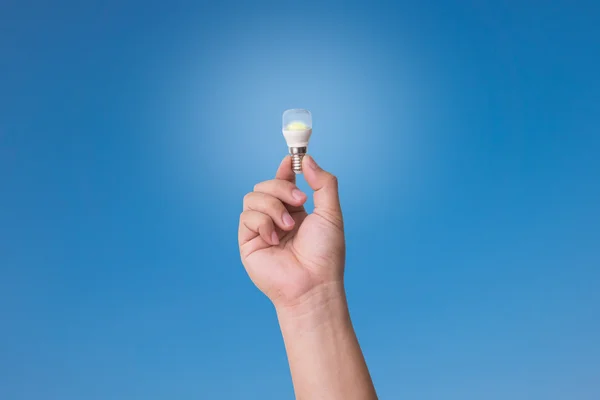 Hand holding LED Bulb with Lighting on blue sky background.