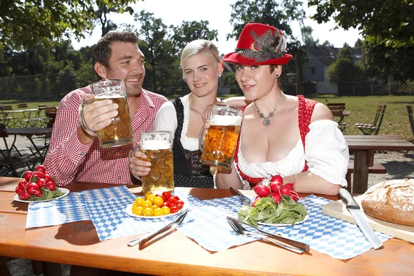 Three Bavarians in traditional costumes sitting in a beer garden