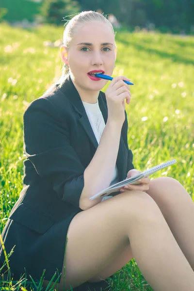 Young woman sitting on the grass and writing in a notebook