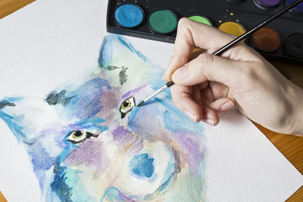 The artist paints a picture Wolf using brush and watercolor colorful painting set.