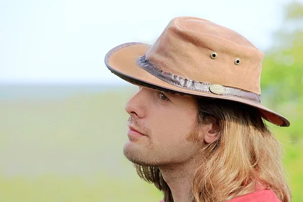 Close-up portrait of handsome guy with long hair in cowboy hat. Safari. Romance. Country style.