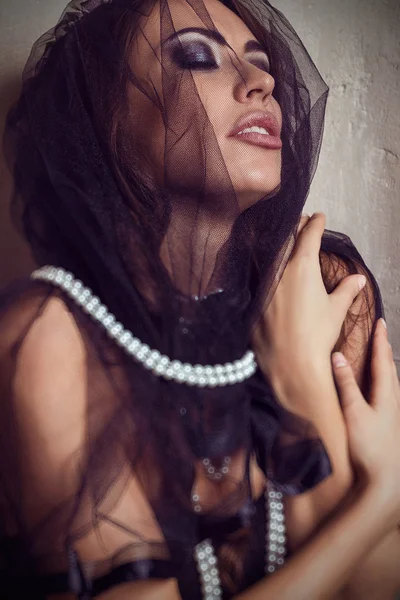 Portrait of beautiful come-hither woman in black transparent lace veil. Accessories white pearl necklace, bracelets. Fashion make-up smoky eyes. Black and white shades. luxury. Sexuality. Seduction. Sensuality. Fashion model shooting.