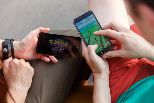 First man held phone in hands showing its screen with Pokemon Go app, second install that application.