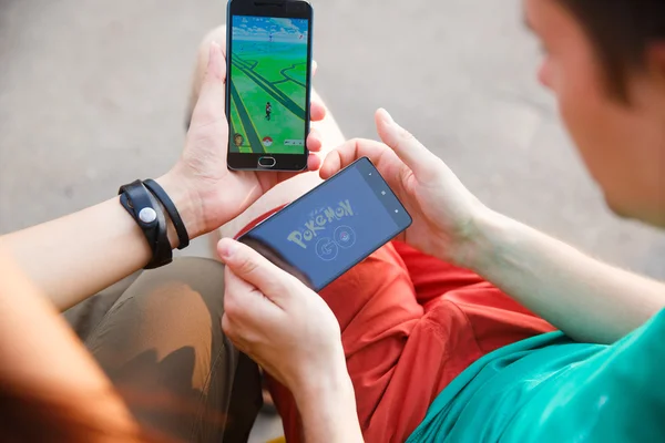 First man held phone in hands showing its screen with Pokemon Go app, second install that application.