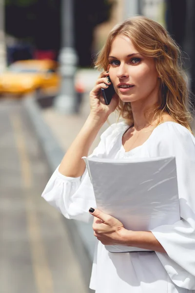 Young woman talking on mobile phone and holding paper