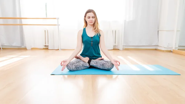 Beautiful young woman sitting on lotus position with closed eyes