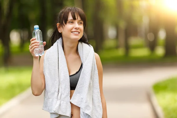 Brunette girl holding bottle of water after sport in park