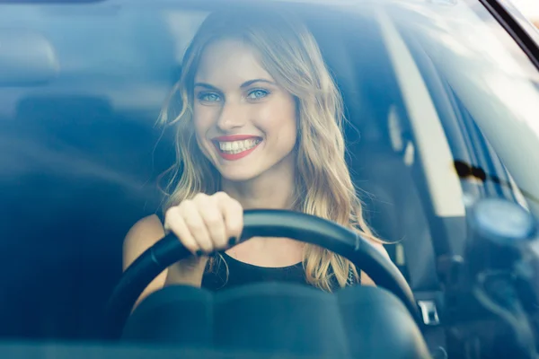 Blond woman with bright smile behind the wheel of car