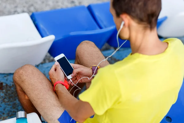 Athlete listening music with phone in hand sitting on stadium