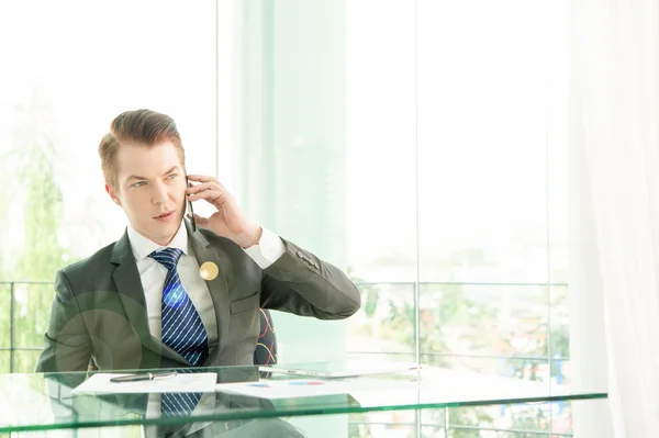 Handsome businessman in suit speaking on the phone in office