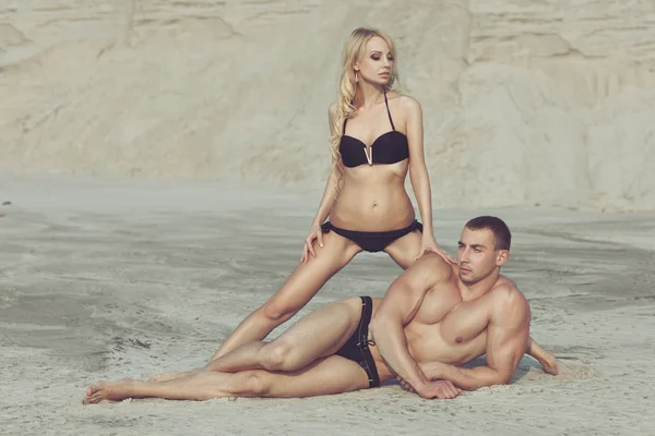 Woman posing with a male bodybuilder on the beach.