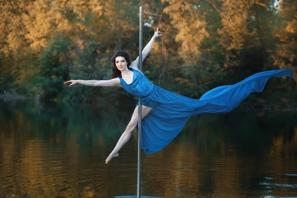 Girl in flowing dress is dancing around a pole dance.